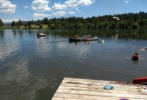 Waterfront at MFC, with two boats in the water and one swimmer in lifejacket. Foreground has edge of dock and lifeguard rescue float visible. 