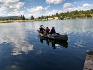 Three people canoeing across the lake, one raising paddle. 