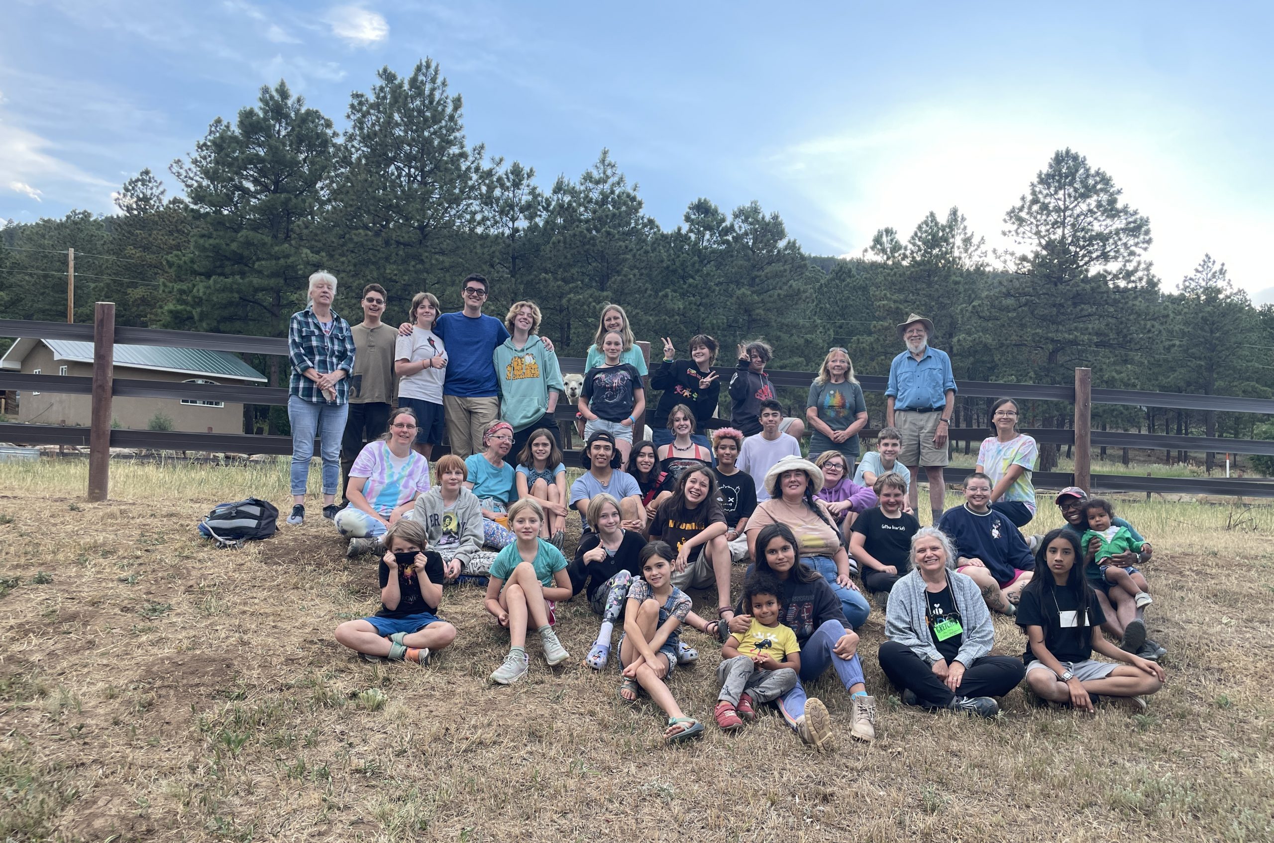 group picture, some sitting and some standing on dry grassy hill. fence, trees in background