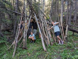 small group of MFCers posing in and around a handmade structure made of fallen branches